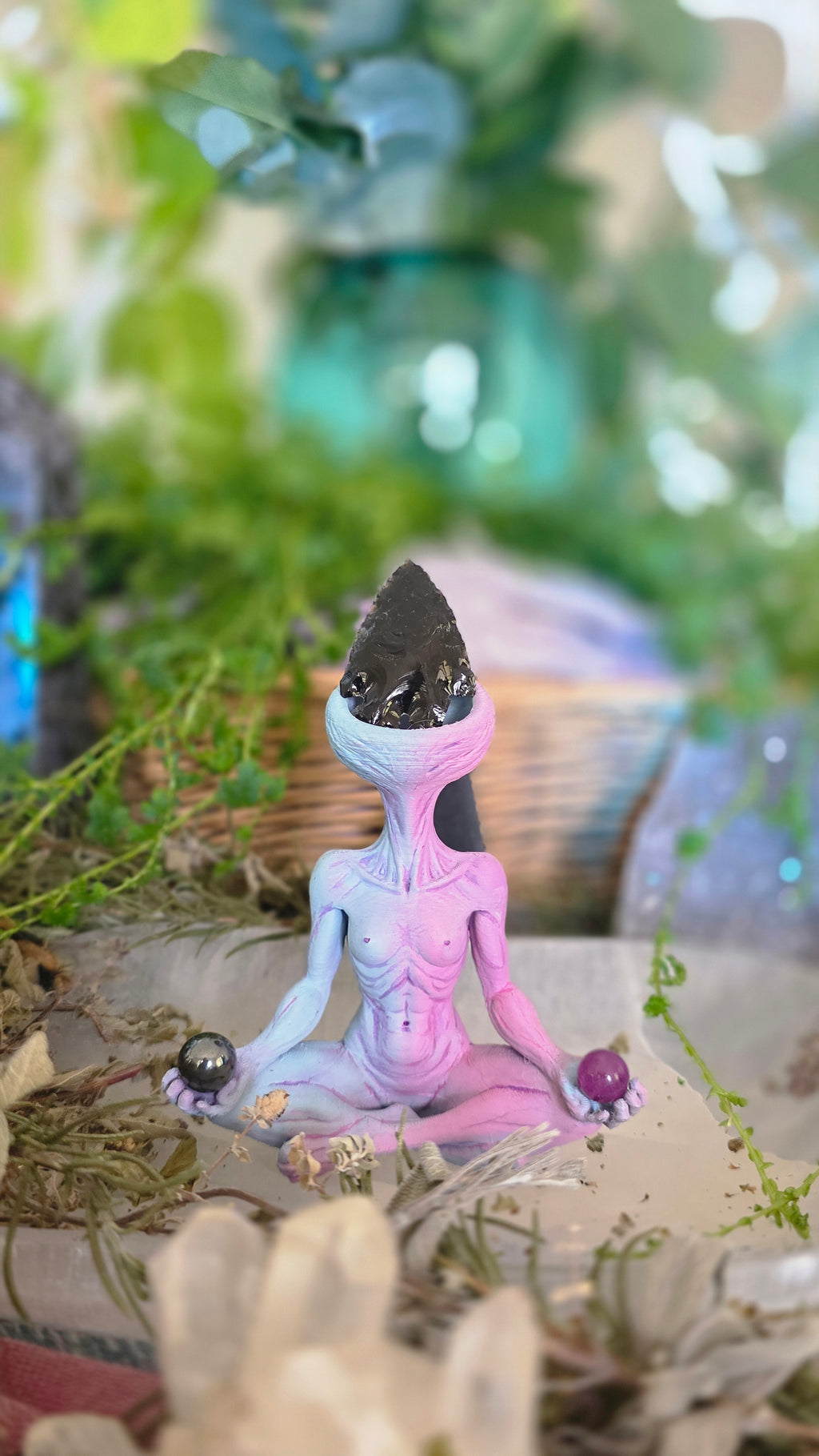 Pink and purple alien figure crstal holder on a tree branch with blurred background