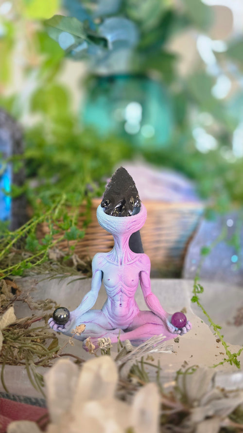 Pink and purple alien figure crstal holder on a tree branch with blurred background