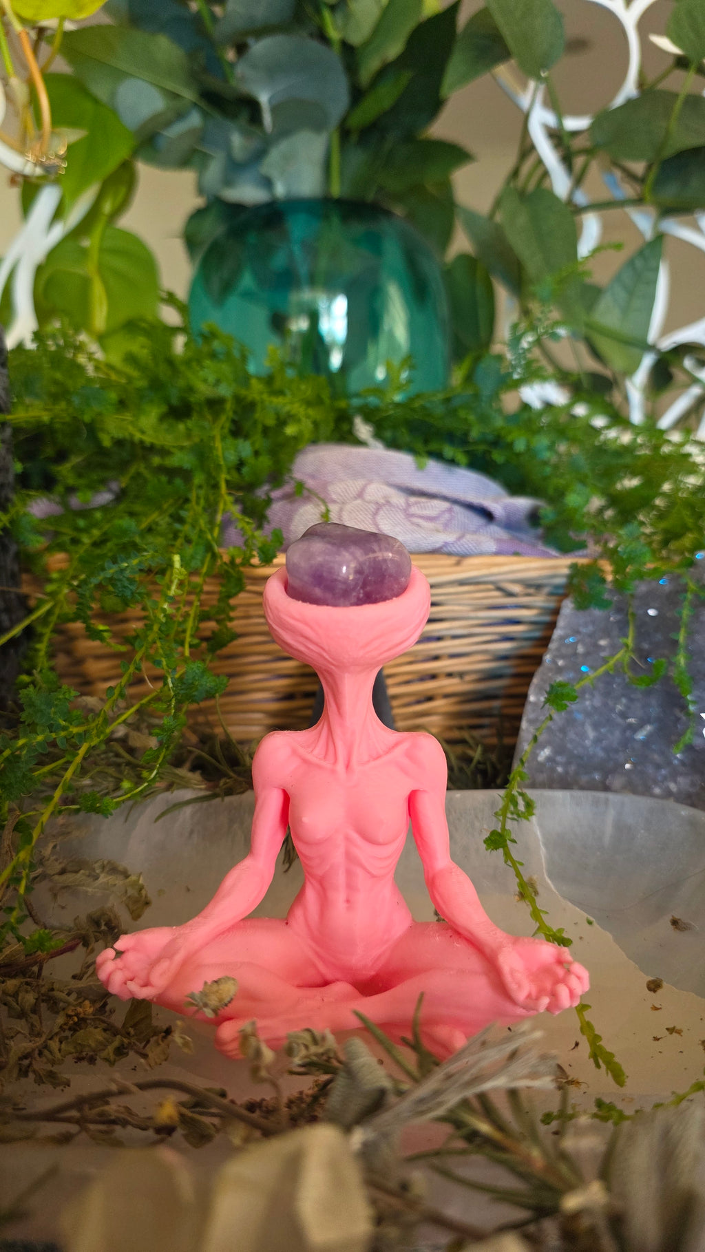 Pink figurine with a purple sphere amidst green plants