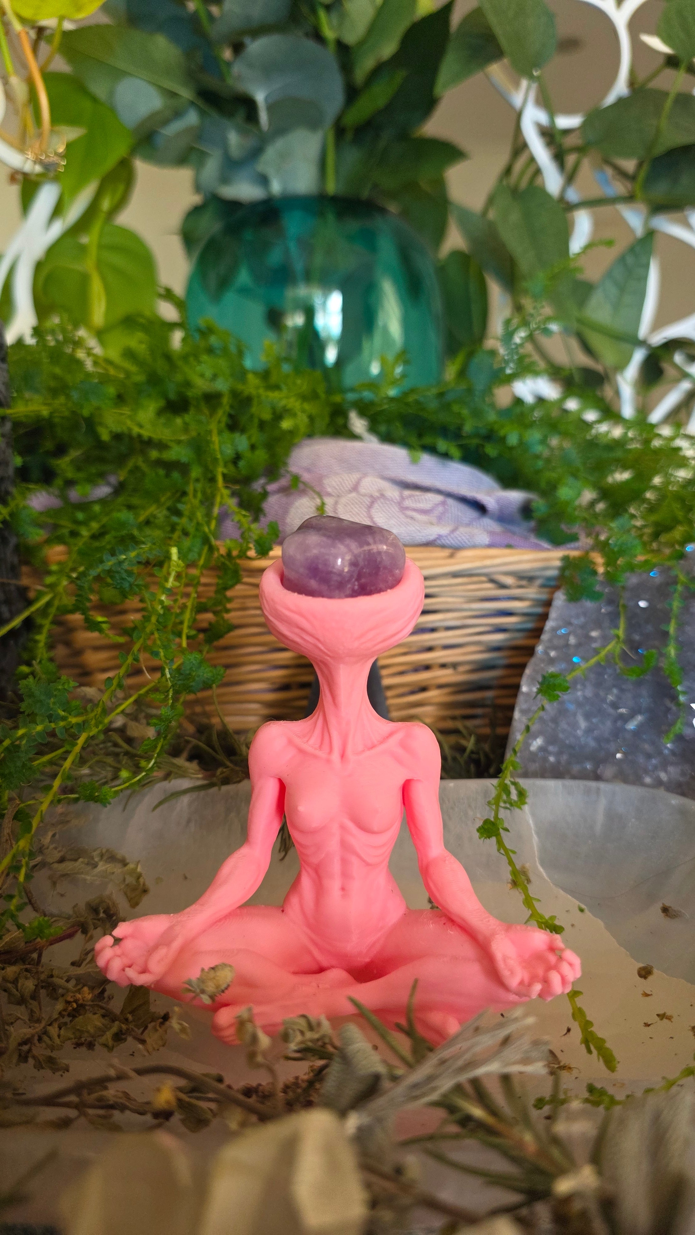 Pink figurine with a purple sphere amidst green plants
